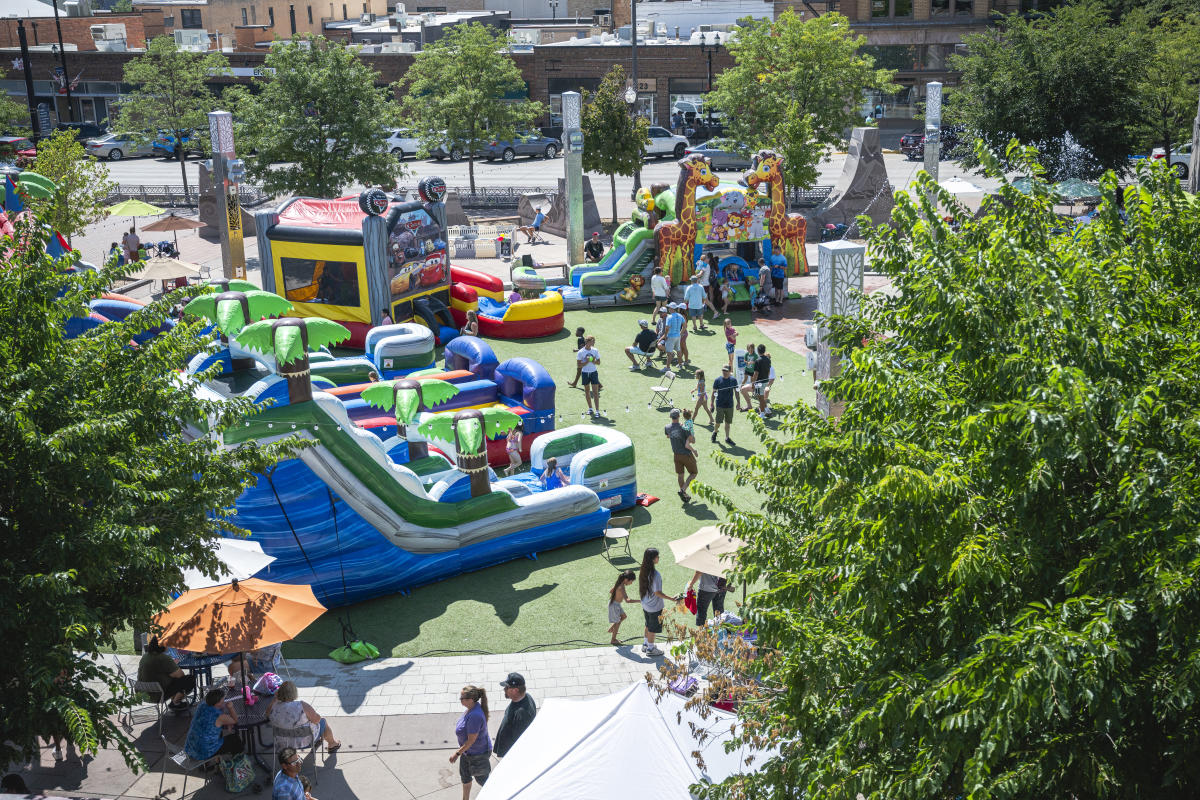 Aerial view of families enjoying colorful inflatable slides, bounce houses, games, and vendor tents during the Back To School Block Party at Main Street Square in Downtown Rapid City.