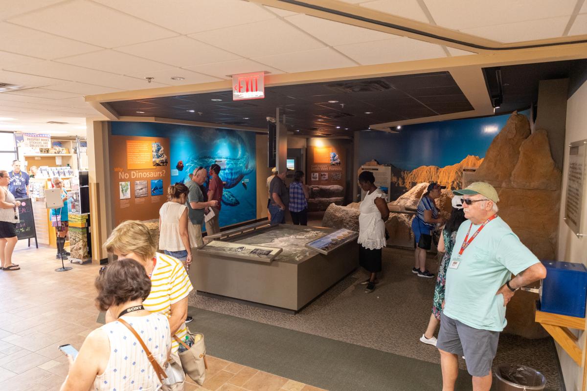 Visitors explore interactive exhibits inside the Ben Reifel Visitor Center at Badlands National Park. Guests gather around a large topographic display while colorful interpretive panels, fossil exhibits, and a model of the Badlands landscape showcase the region’s geology, ancient ecosystems, and natural history.