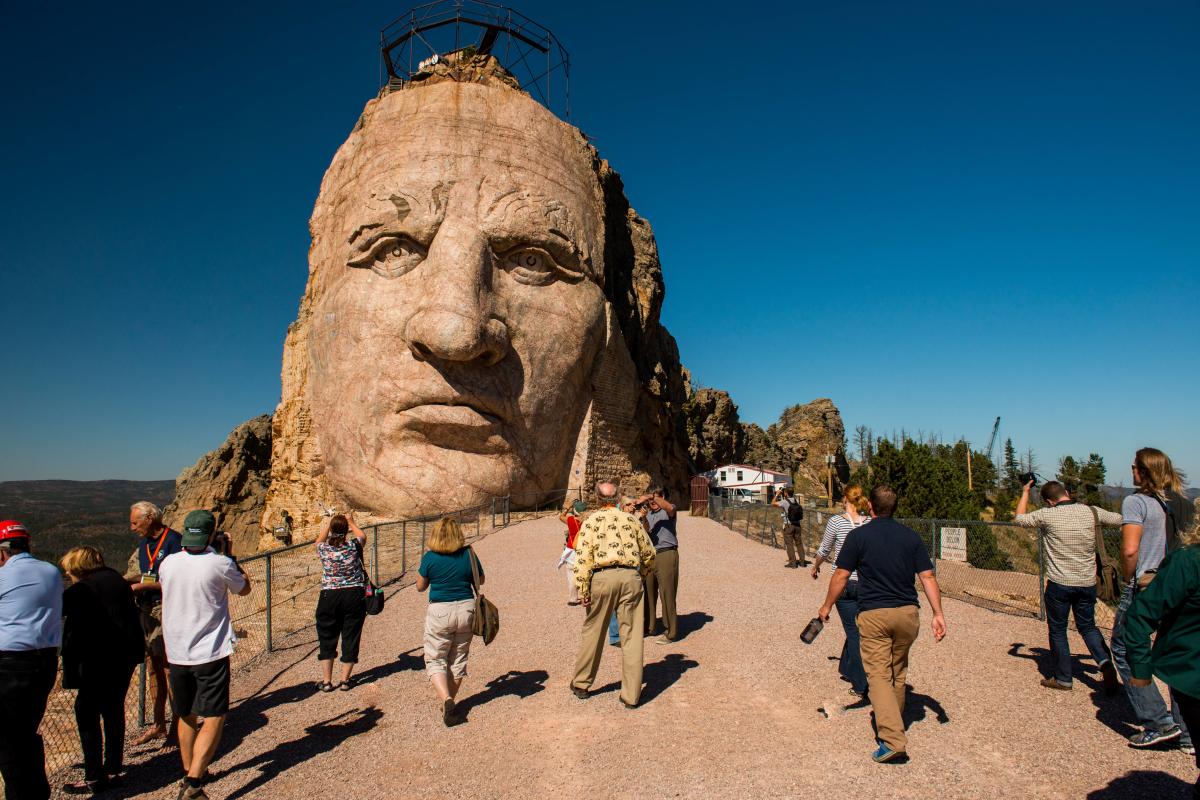 Upclose image of Crazy Horse's face, with people walking around taking photos.