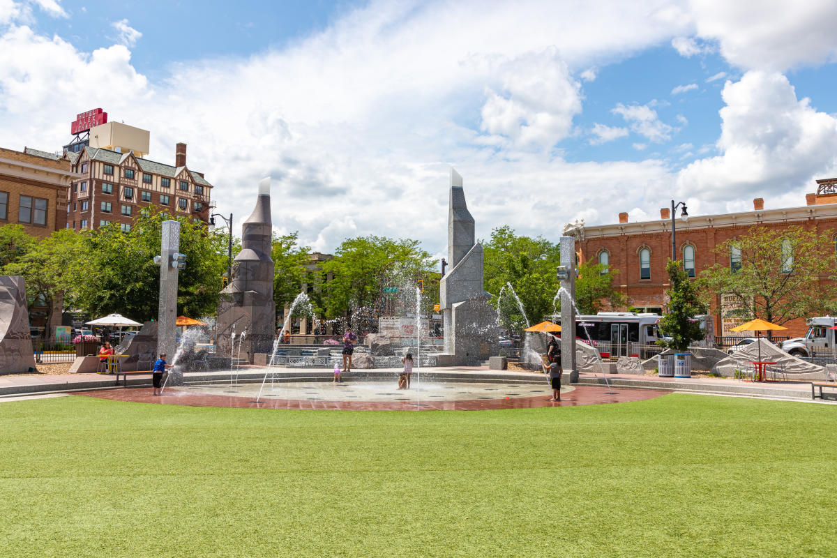 Green grass and an interactive splash patio surrounded by historic buildings in downtown Rapid City, SD.
