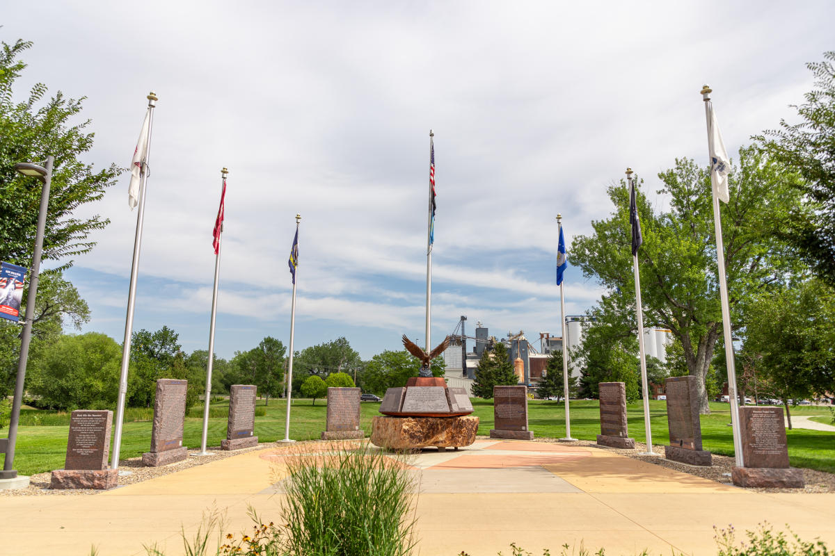 The Black Hills Veterans Memorial in Memorial Park features seven flag poles, with the six military branches surrounding the courtyard and an American flag in the center above a stone monument.