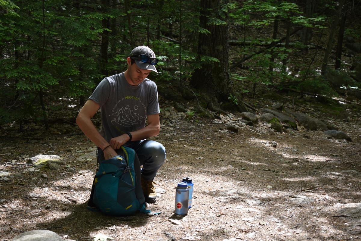 Man packing backpack with water bottles next to him on hiking trail in the Black Hills