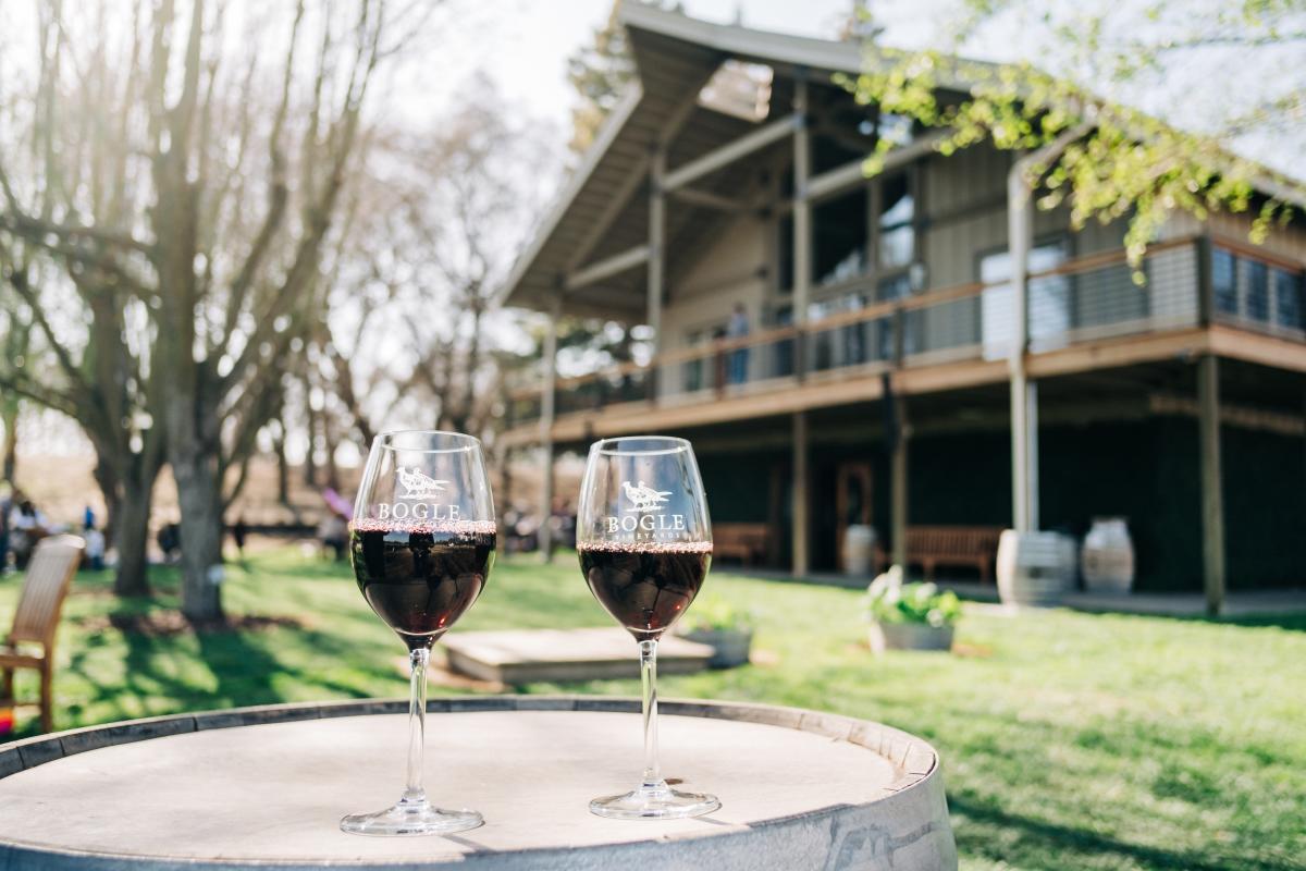 Two glasses of red Bogle wine on a wine barrel with the building in the background.