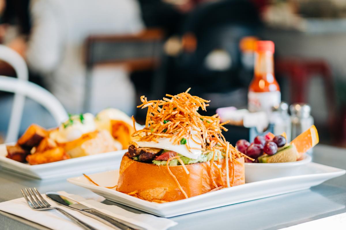 A B&B Burger from Bacon and Butter with a side of fruit and more food in the background on a white tray.