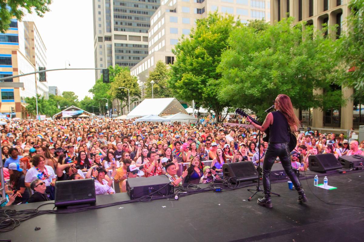 A guitarist performing onstage for a crowd of of cheering fans at a street festival