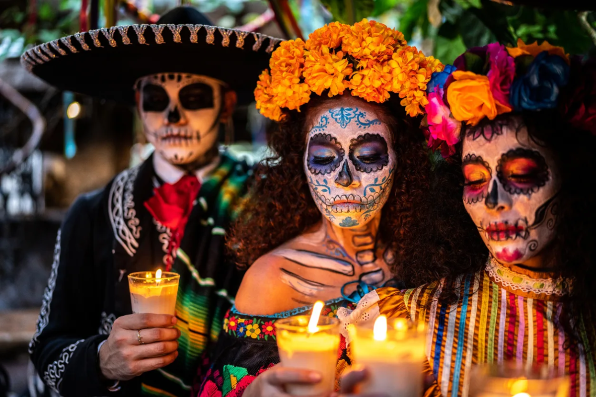 Celebrants wearing colorful dresses and suits with intricate face paintings of skulls
