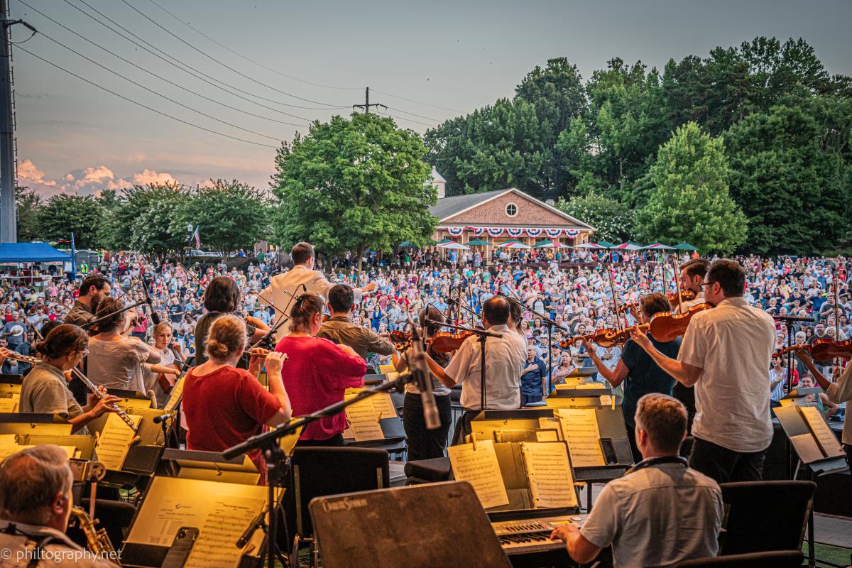 Symphony playing in front of large crowd in park for the 4th of July