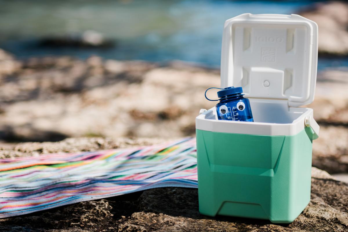 A cheeky reusable container peeks out over the edge of a personal cooler on the banks of the San Marcos River