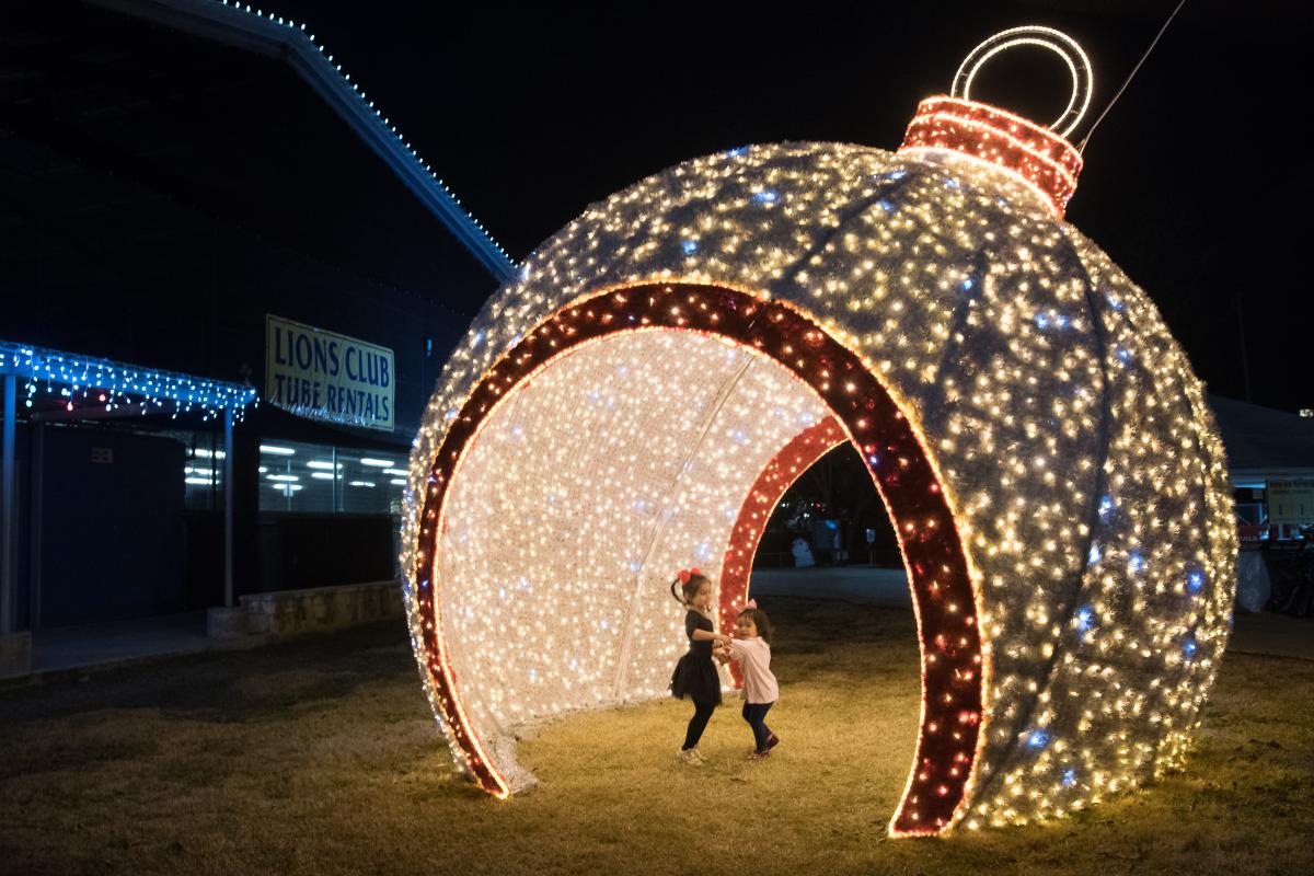 Two little girls dance under a light display at Sights & Sounds of Christmas in San Marcos Plaza Park in San Marcos, Texas