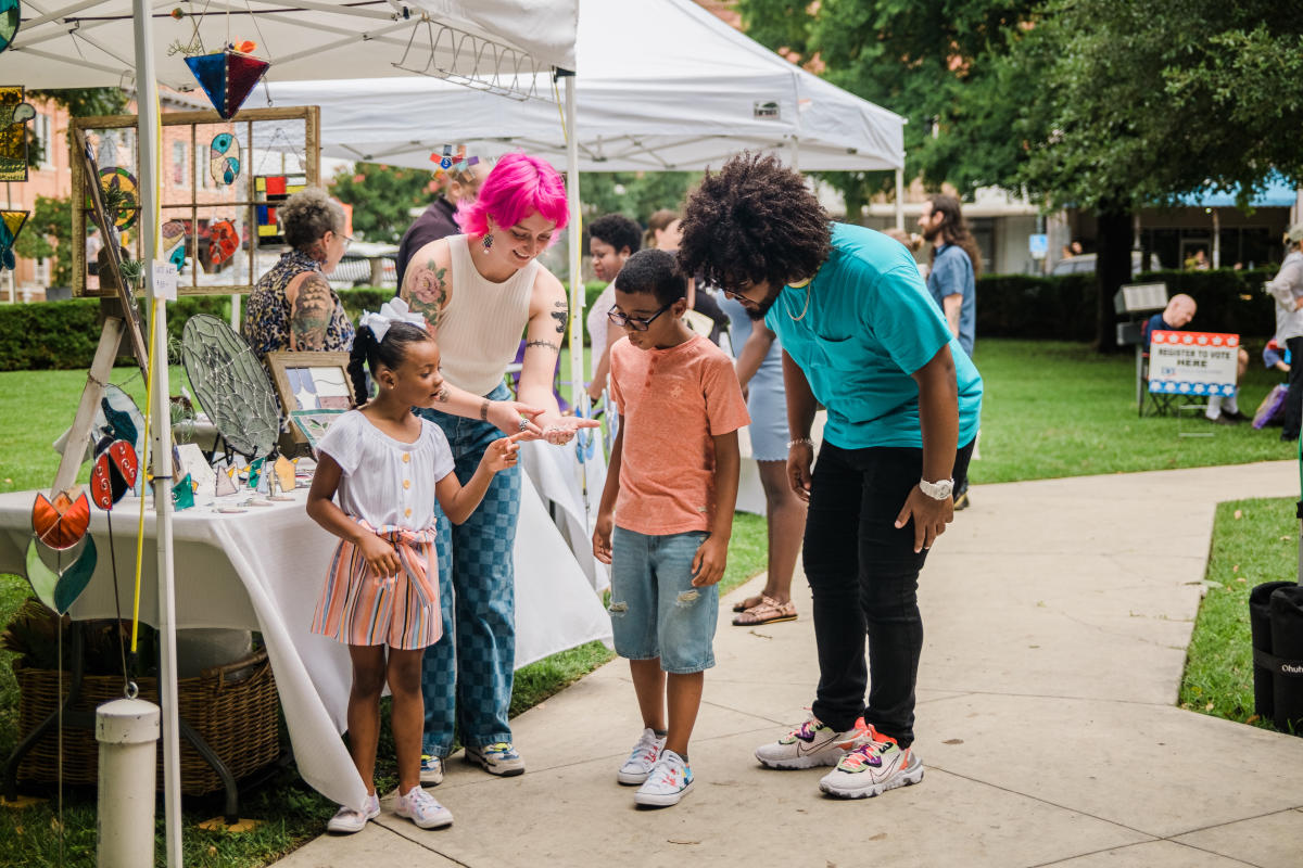 Woman shows man and kids a piece of art at Art Squared in Downtown San Marcos, TX.