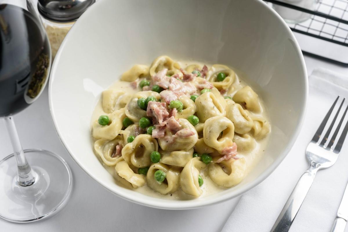A photo of Giuseppe's Pastacaffe's tortellini next to a glass of wine and a fork
