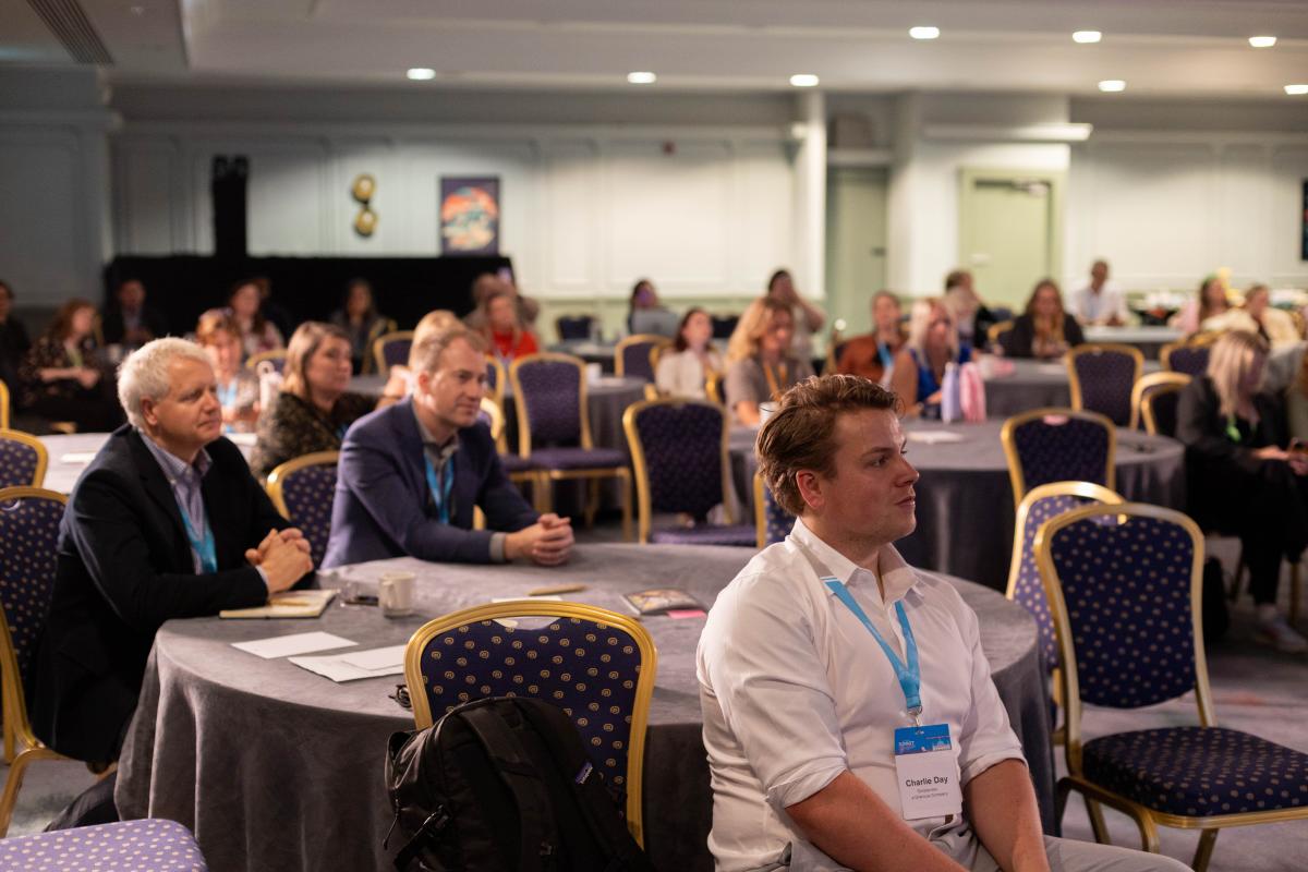 Attendees sit at conference tables and watch a presentation during a EMEA Summit.
