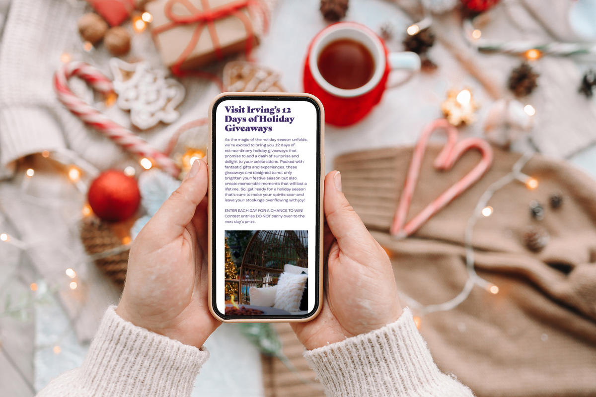 Holiday themed items sit on a table as a person views Visit Irving's 12 Days of Holiday Giveaways on a phone.