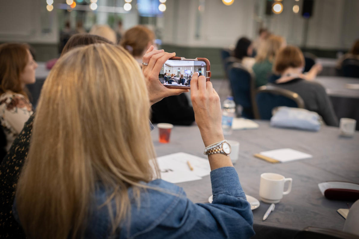 An attendee at EMEA Summit holds up their phone to take a photo during a session.