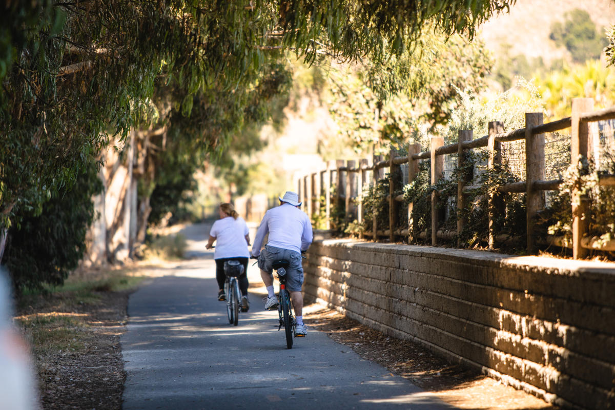 two people riding bikes along a paved path