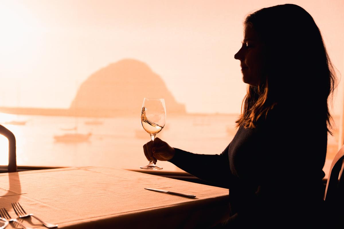 Women at table swirling wine with Morro Rock in background