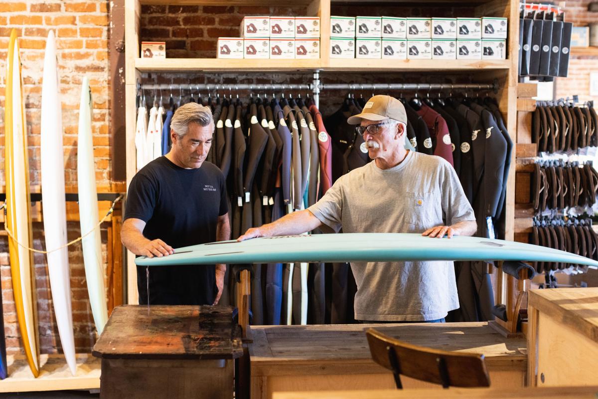 man showing another man the work that was done on their surfboard