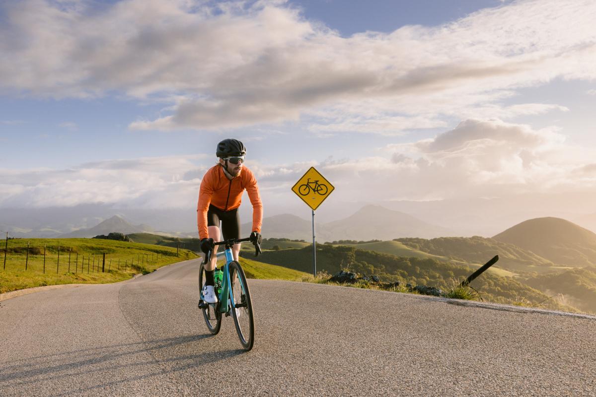 Man biking on a road through green hills with blue sky and clouds above