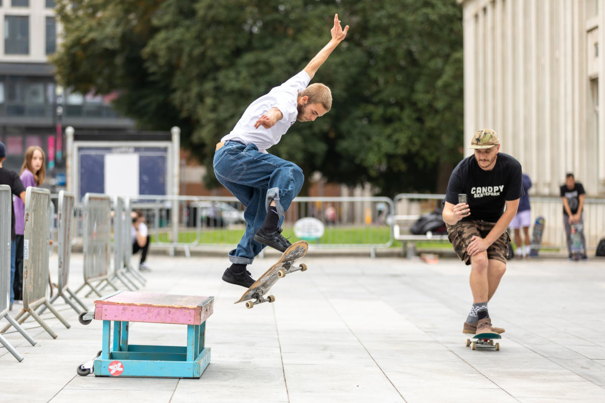 Man jumping in air with skateboard as another skateboarder films trick
