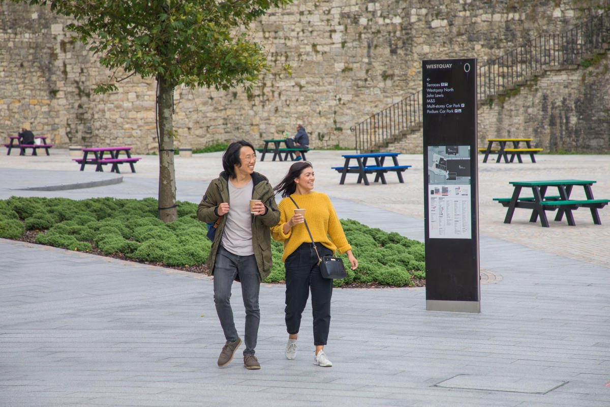 Man with backpack and women holding a coffee cup walking around Westquay Esplanade
