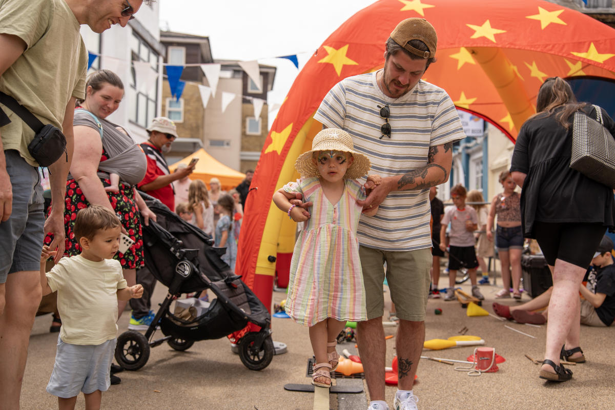 Father holding daughters hands as she enjoys circus workshop activities at Bedford Place Summer Festival