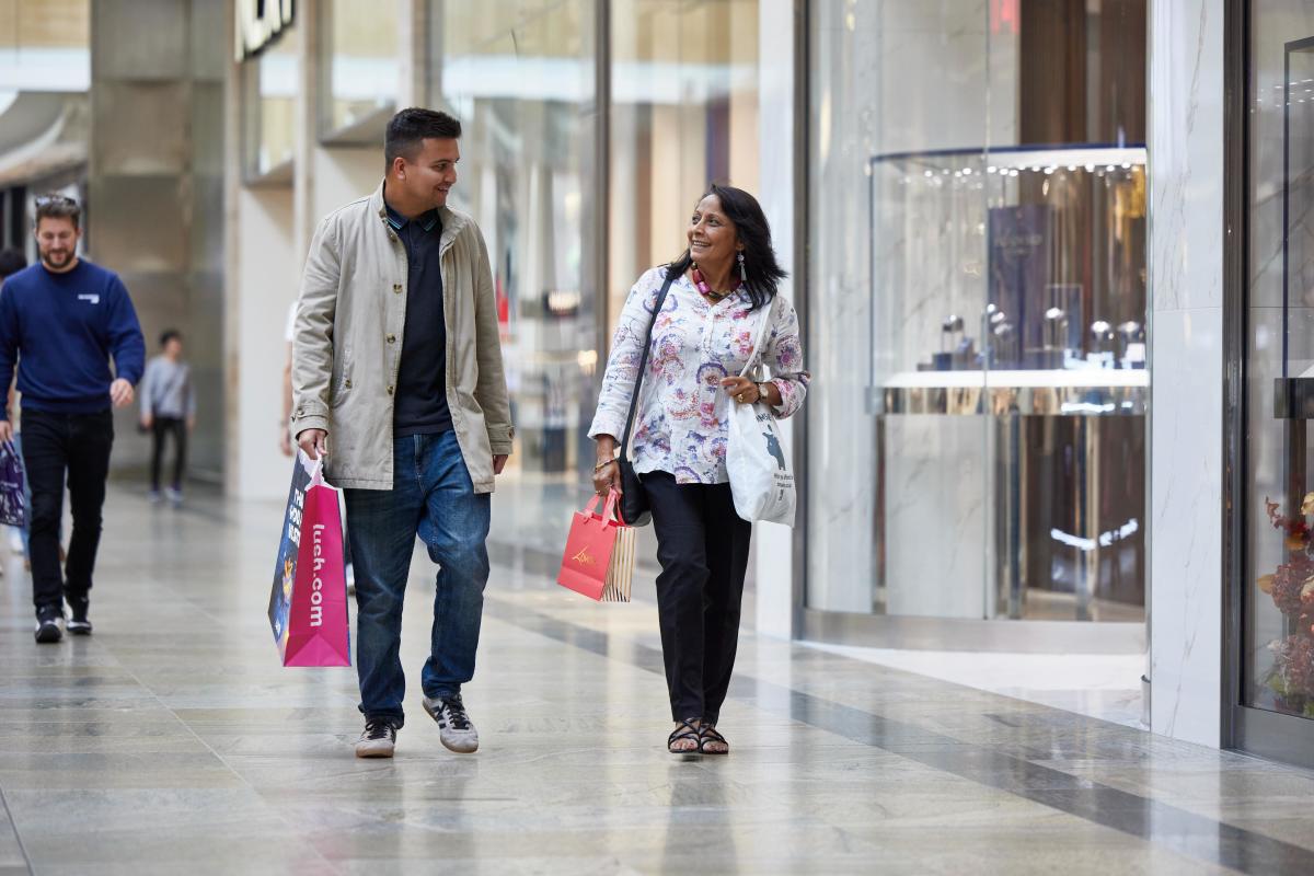 Two people walking towards camera inside Westquay Shopping Centre holding shopping bags and smiling