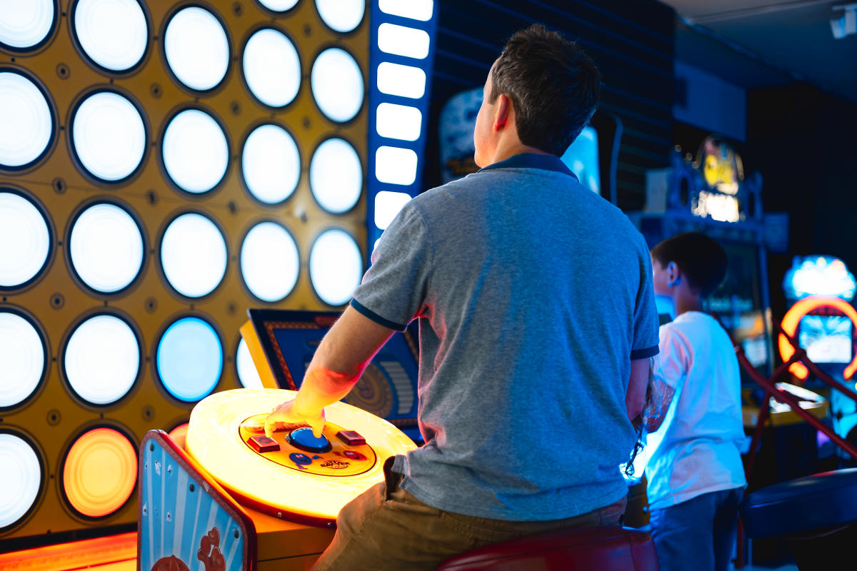 Father and son sat side by side playing arcade game at High Score Arcades