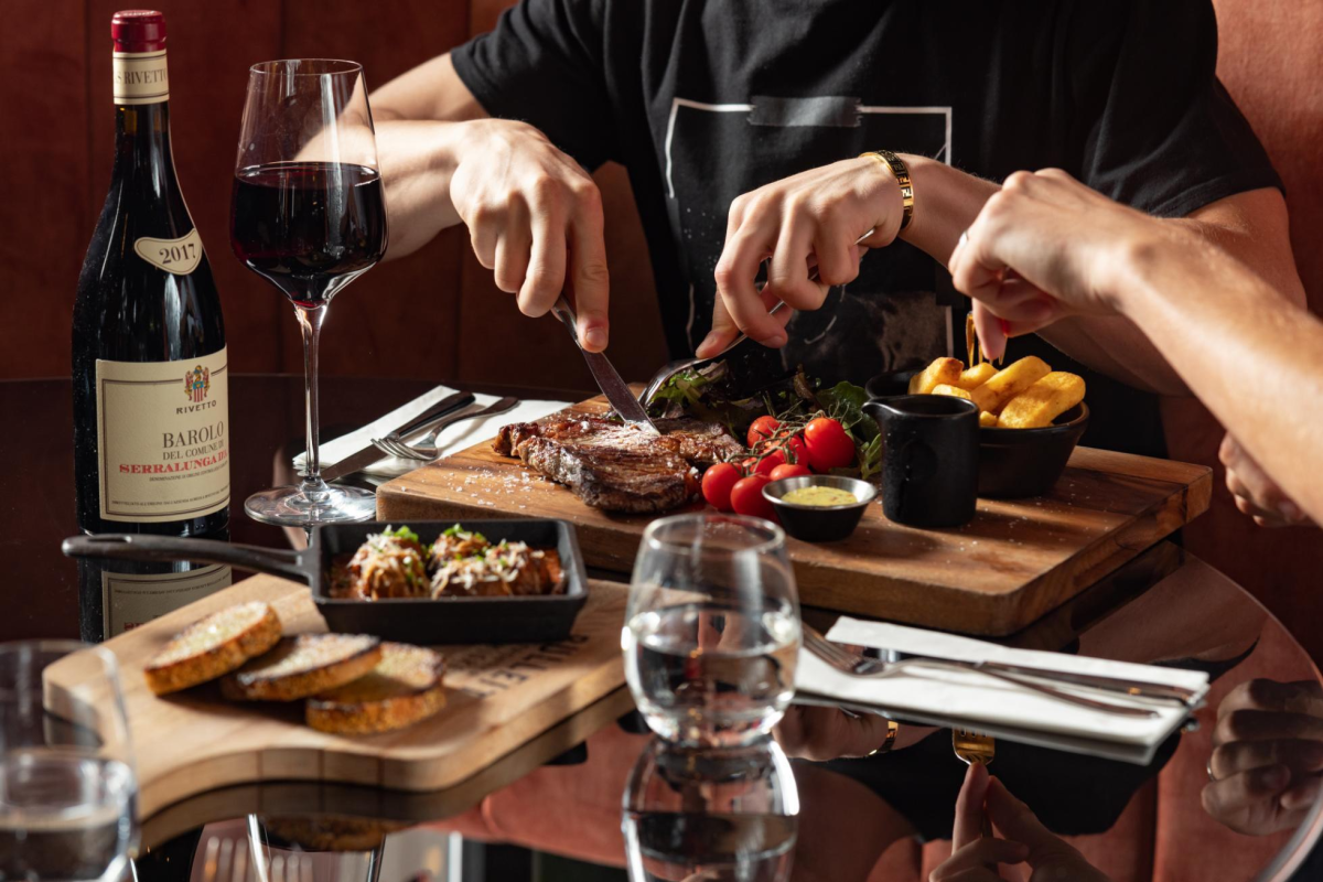 Man eating steak from cutting board paired with chips and vine tomatoes and wine