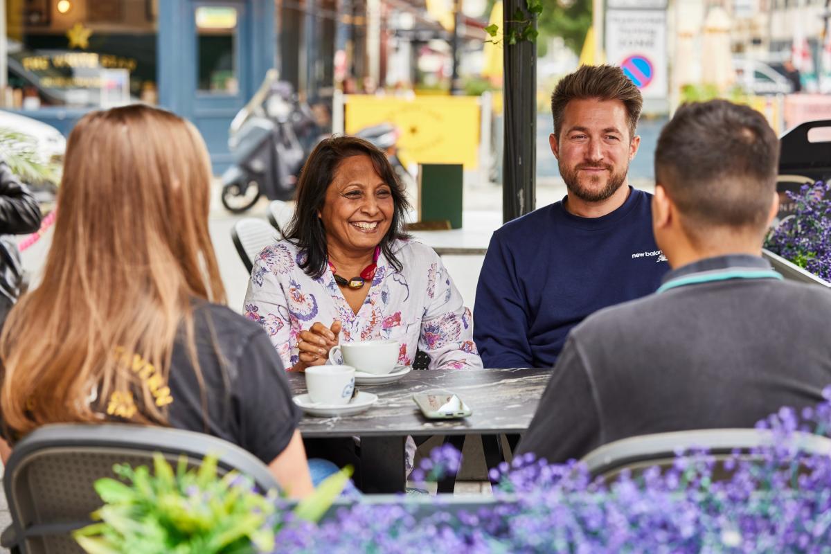 Four people sat around a table outside in Oxford Street drinking coffee and talking