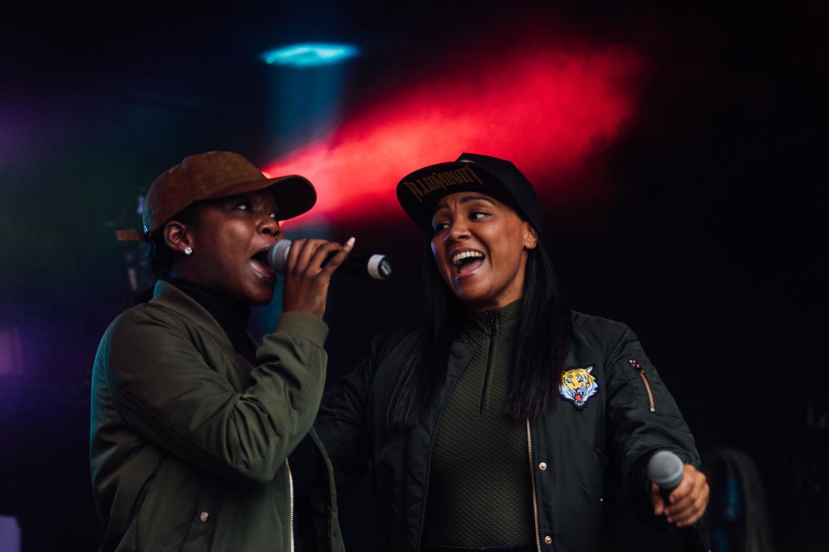 Two women wearing baseball caps holding mics on stage
