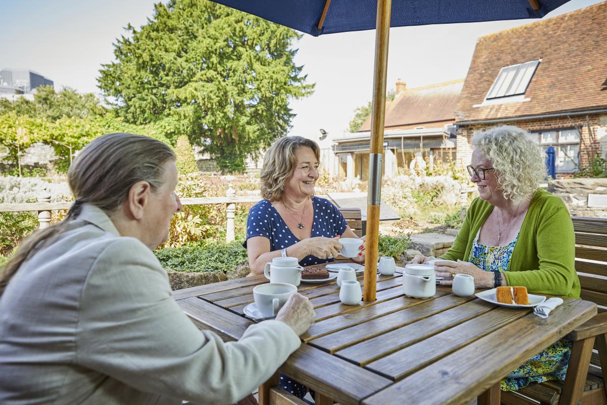Group of friends enjoying teas and cakes outside on a picnic bench in Tudor House Gardens