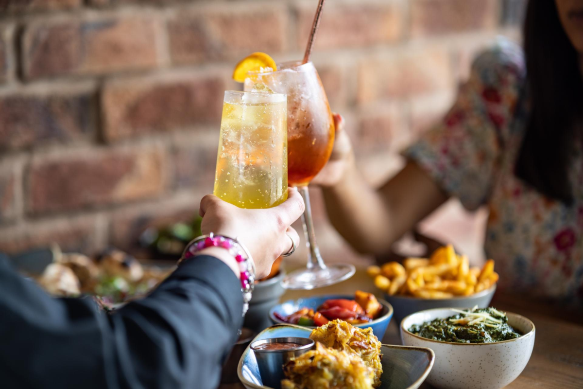People going cheers with two colourful drinks at Tap & Tandoor