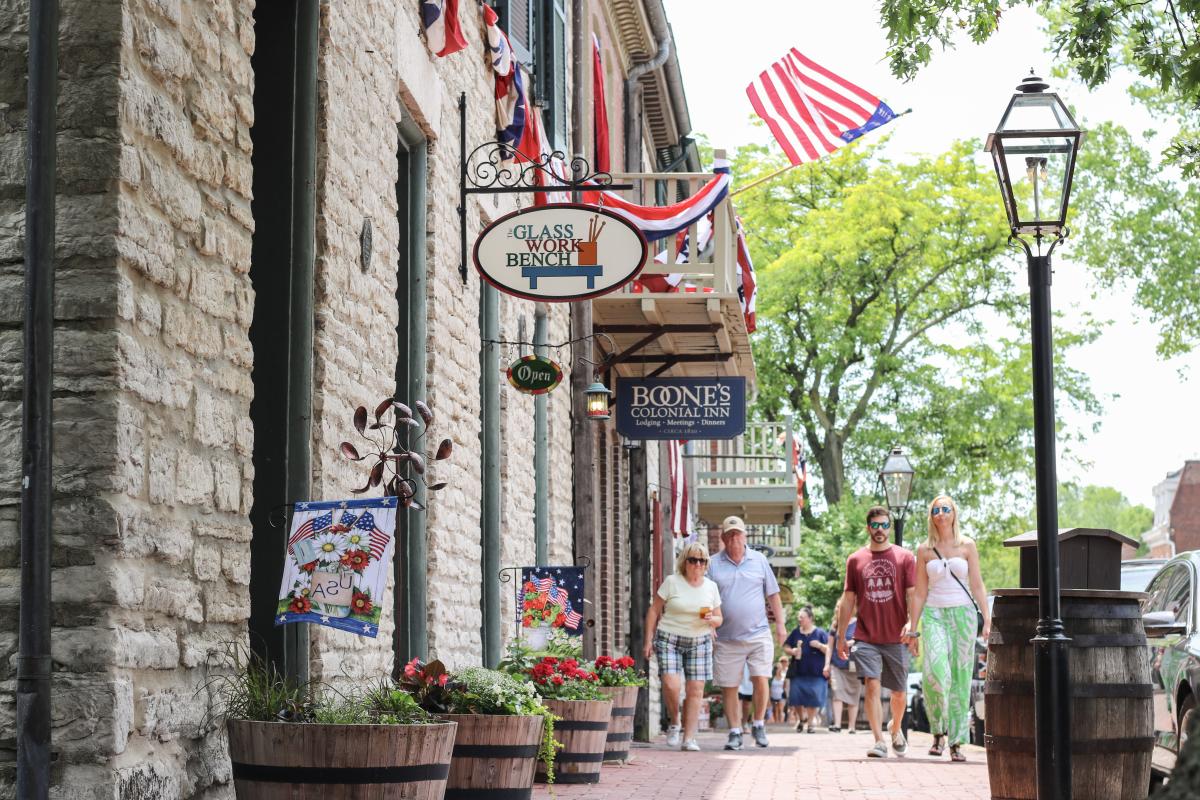 Pedestrians walk past historic stone buildings and American flag decorations on Main Street in St. Charles, Missouri.