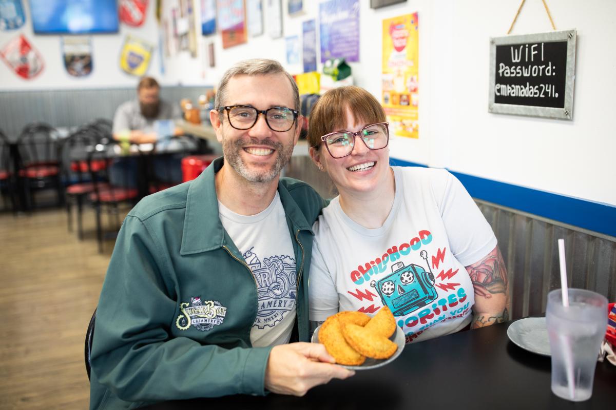 Man and Woman holding up plate of empanadas at restaurant