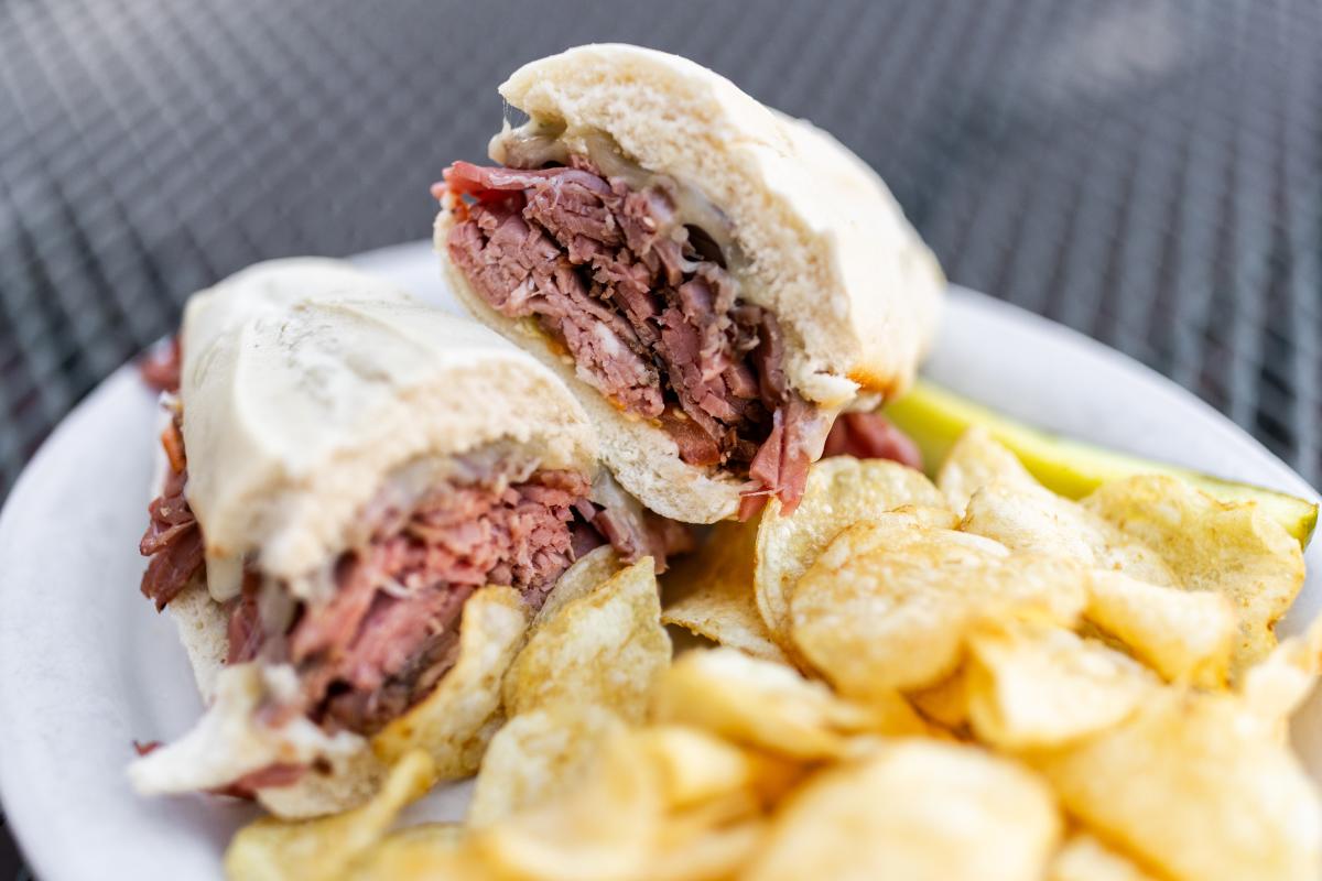 sandwich with white italian roll, beef, and cheese, sitting atop bed of potato chips, with a dill pickle visible to the side