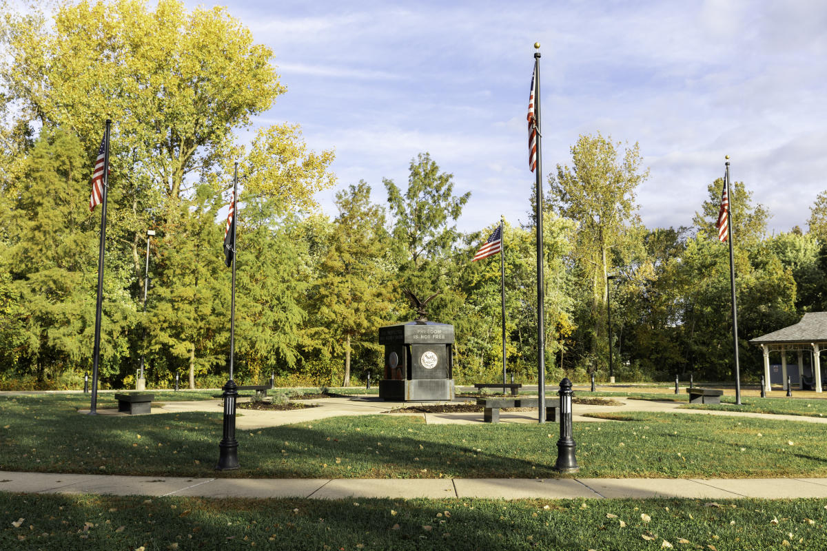 The St. Charles, Missouri Veterans Memorial surrounded by American flags and tall trees.