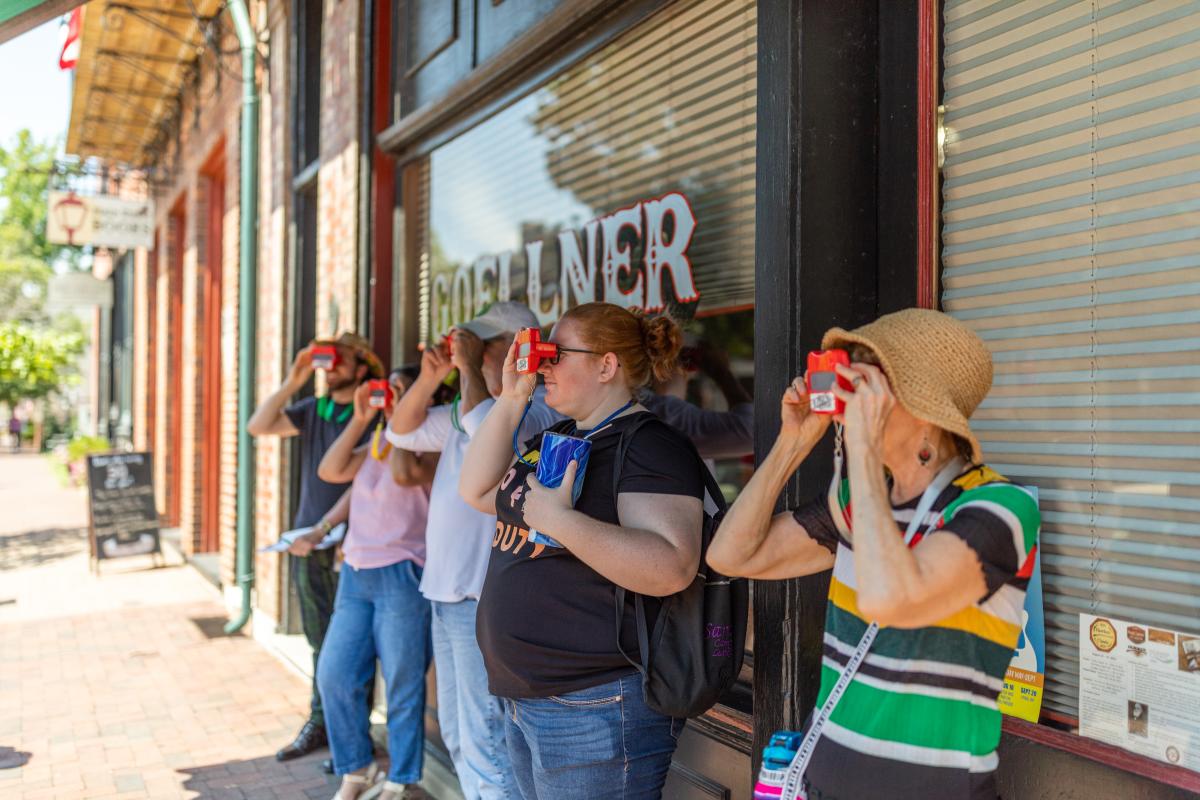 A group of people looking through ViewMasters on a Hit the Bricks walking tour on Historic Main Street in St. Charles, Missouri.