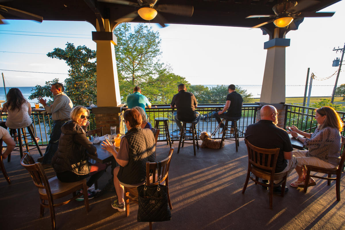Guests of The Barley Oak, and their dogs, seated around tables on the second floor balcony overlooking Lake Pontchartrain.