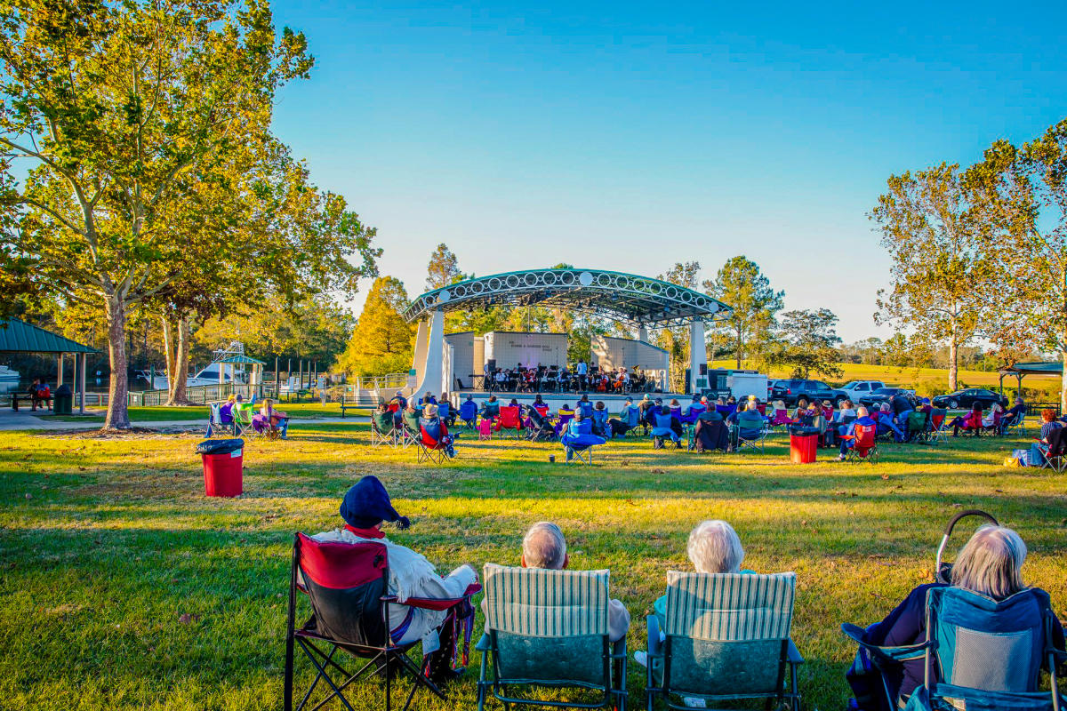Audience members relax in lawn chairs on the grass at Heritage Park in Slidell during a Bayou Jam concert, with musicians performing on the Ronnie A. Gardner Sr. Stage.