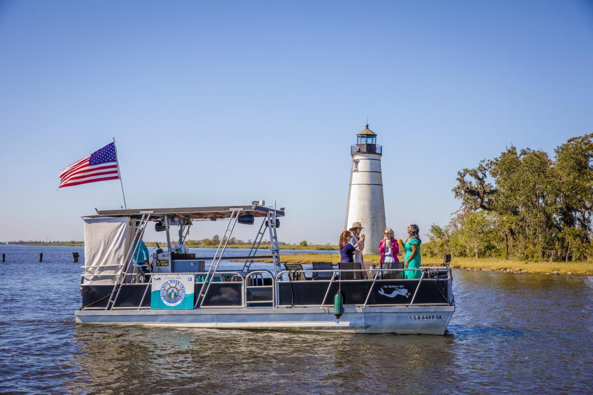 Guests ride a pontoon boat on the Tchefuncte River with the historic Tchefuncte River Lighthouse in the background during a Tchefuncte River Charters excursion.