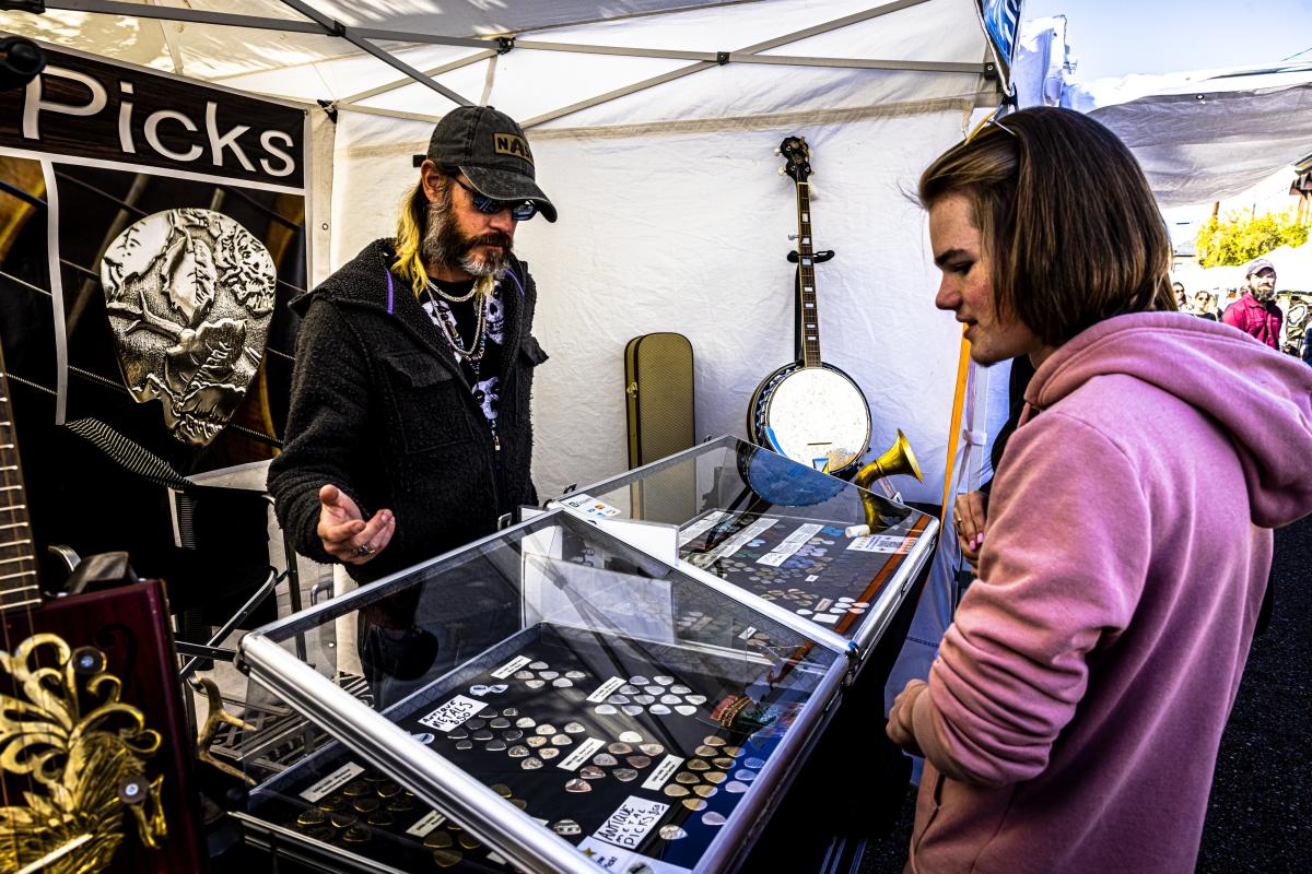 A man shows handmade guitars and accessories to a young shopper in his booth at the Covington Three Rivers Art Festival.