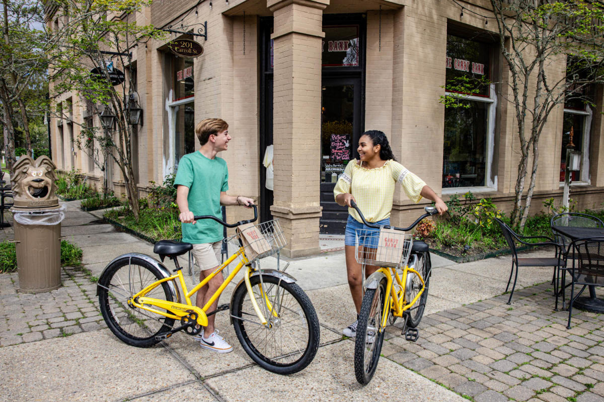 A young man and young woman each stand beside a yellow bike, in front of The Candy Bank in Old Mandeville.