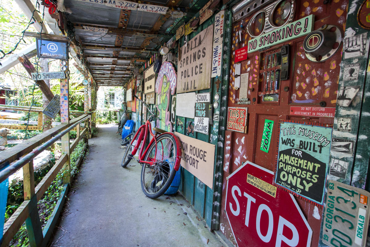 An exterior view of the Abita Mystery House, a roadside attraction in Abita Springs, Louisiana, a rambling series of buildings filled with oddities, collections, handmade and vintage signs, interactive dioramas and toys, and classic arcade games.