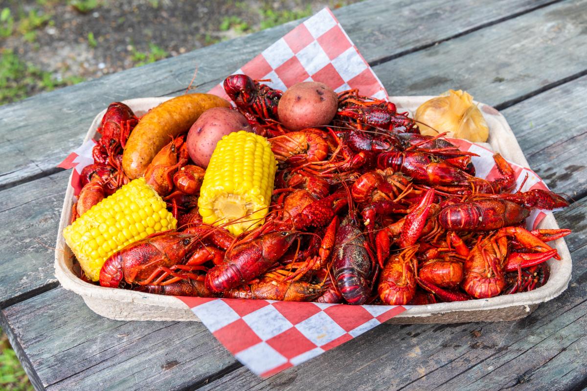 A tray of boiled crawfish with all the fixings rests on a weathered, gray picnic table at Bayou Boil-n-Go in Covington.