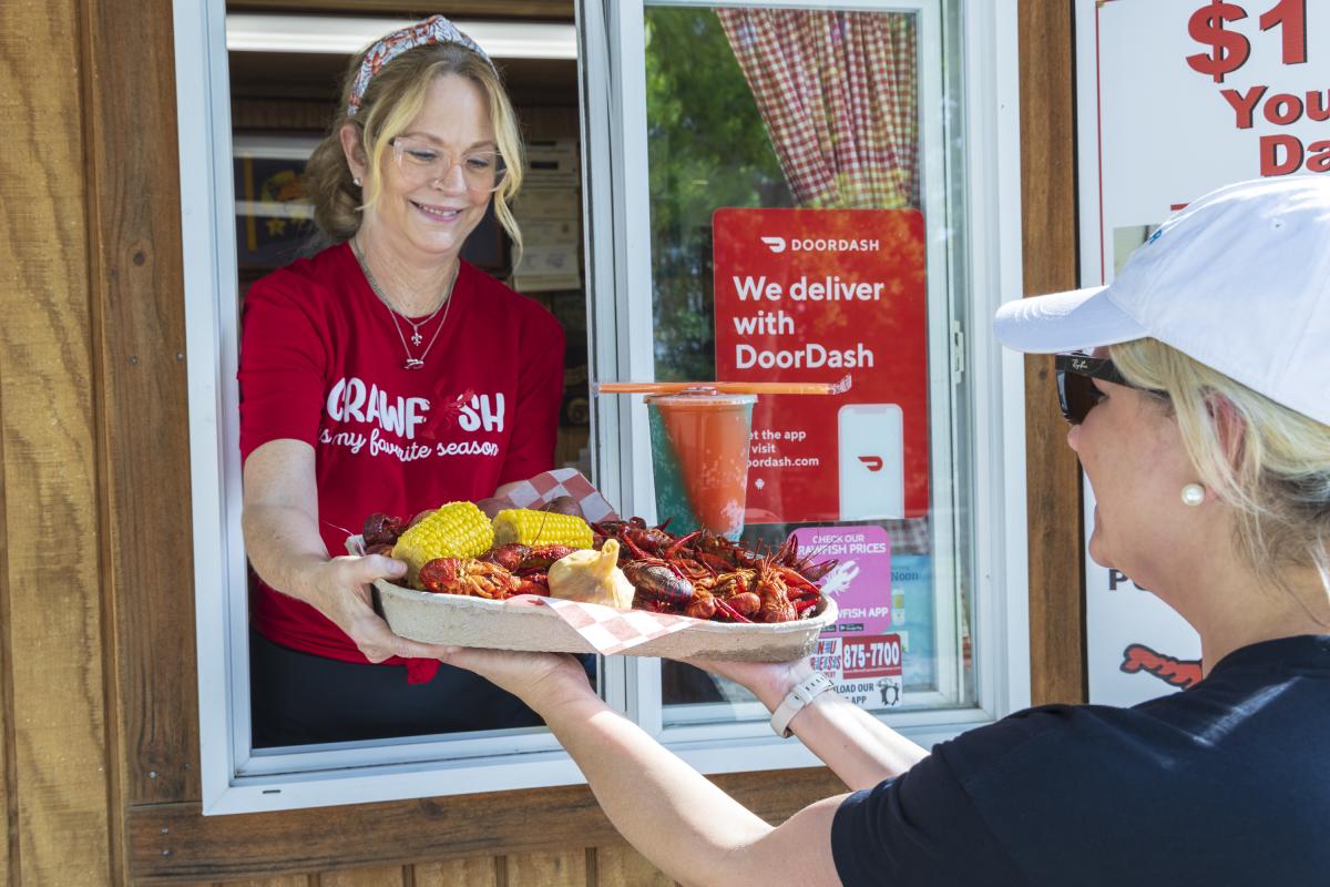 At Bayou Boil-n-Go, a woman hands a large tray of boiled crawfish with all the fixings through the take-out window to a customer.