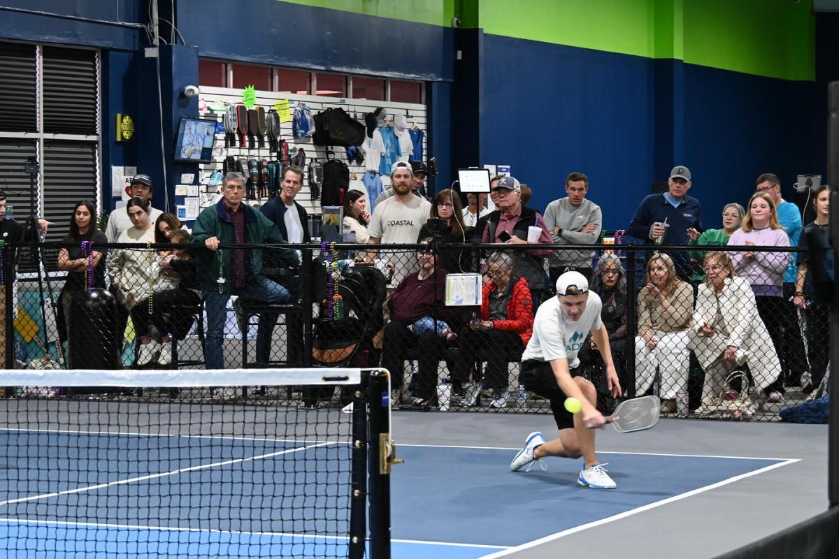 A pickleball player swings to hit the ball as a crowd watches from behind.