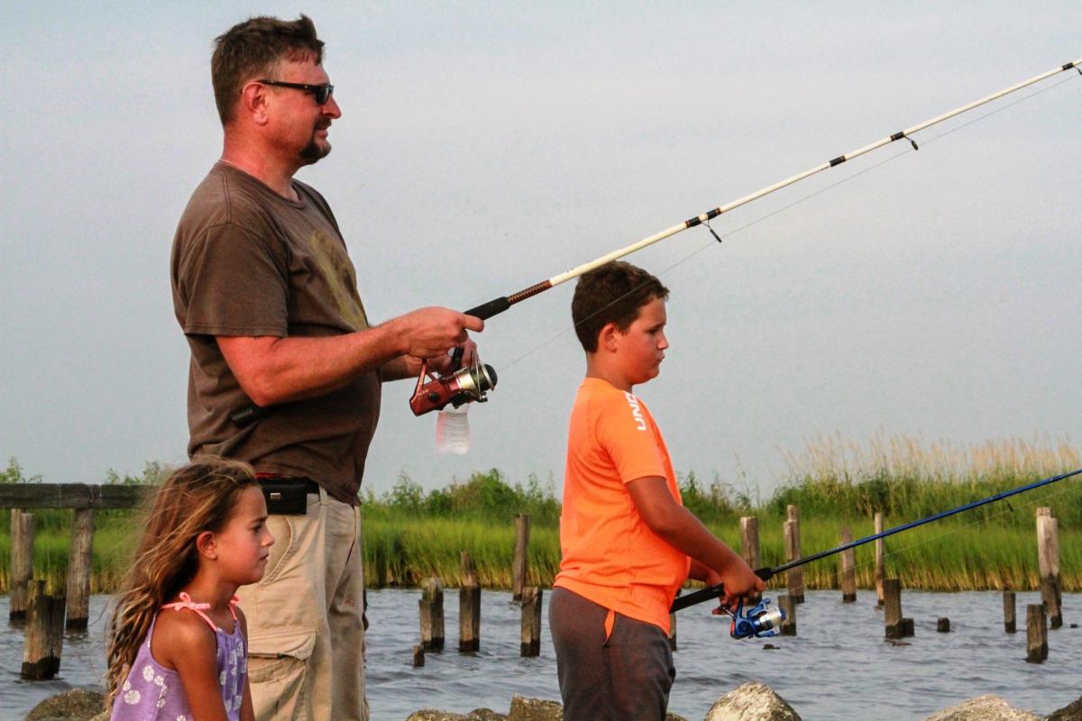 A man, boy and girl fishing on Lake Road in Lacombe with the grassy shore behind.