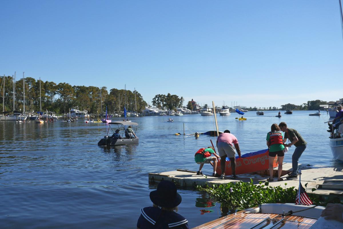 People launch a handmade boat into the Tchefuncte River during the Quick ’n Dirty Boat Building Contest at the Madisonville Wooden Boat Festival, with boats and spectators lining the waterfront.