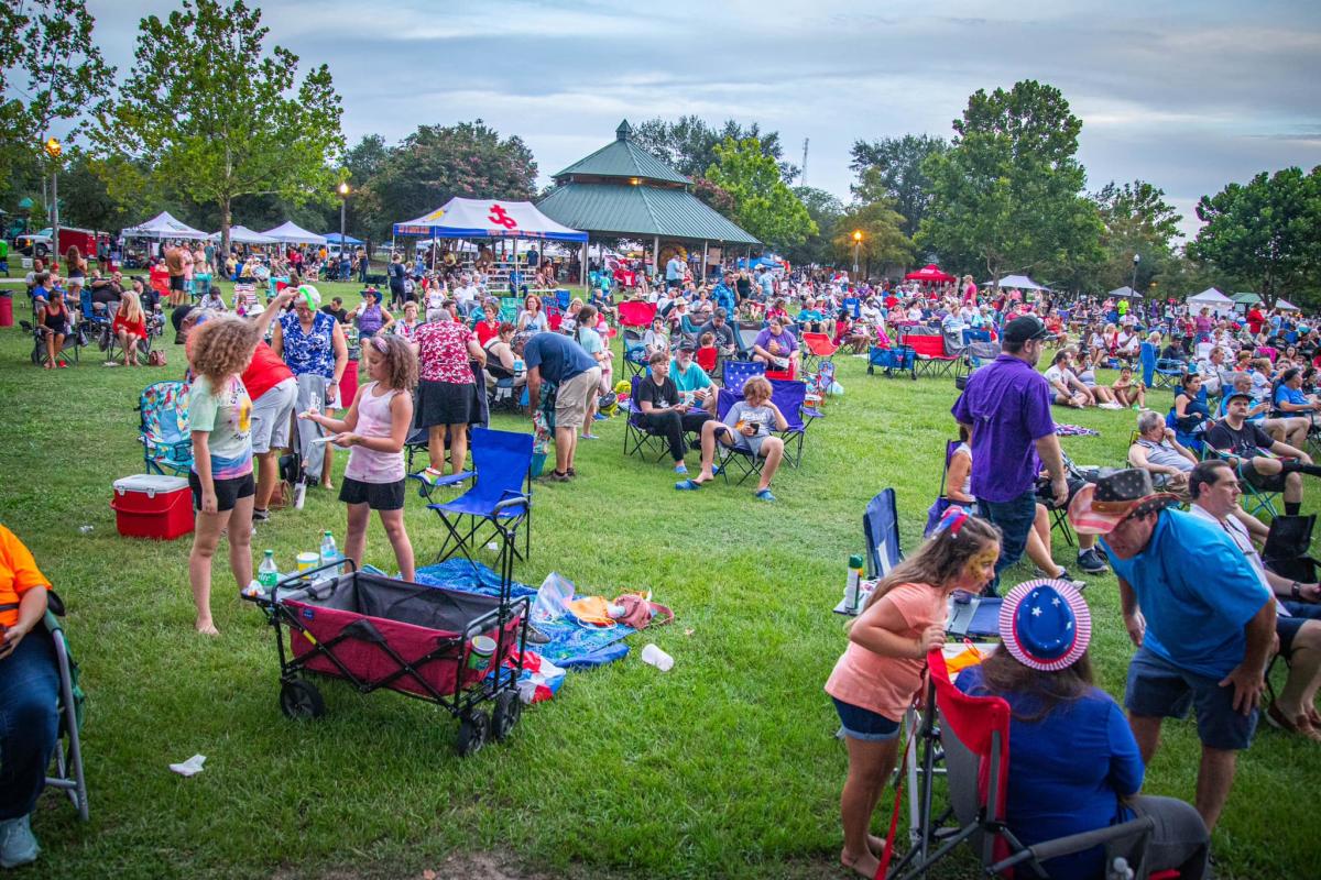 Large group of festival-goers cover the lawn in Heritage Park with lawn chairs and coolers.