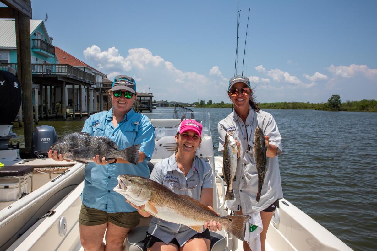 Three women representing Wish to Fish Louisiana stand on a docked boat holding fish caught on a tour with Angling Adventures of Louisiana captain Mike Gallo.